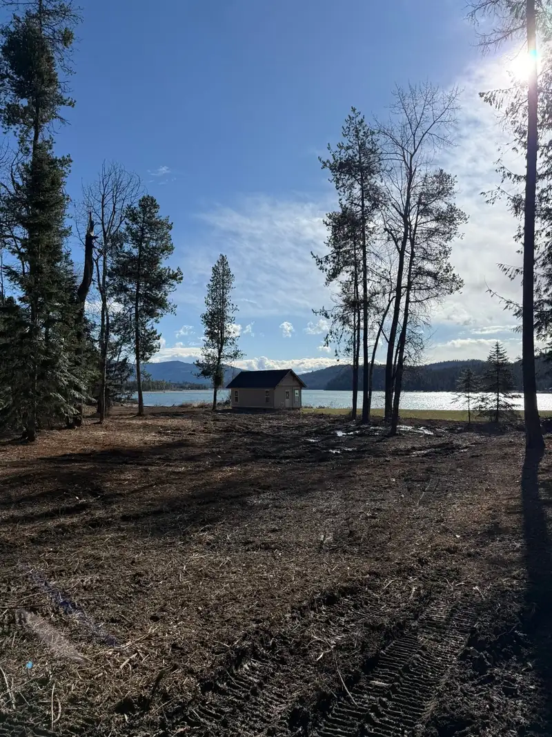 After: the same Lake Pend Oreille property cleared, mature trees left standing and a cabin by the water