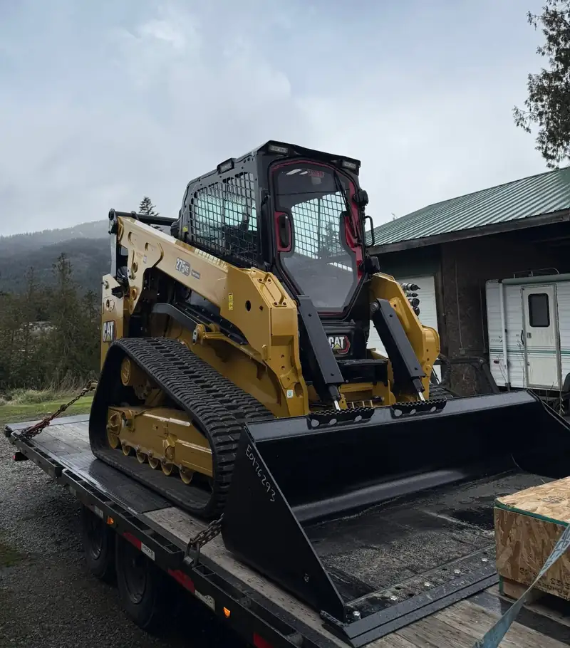 CAT tracked loader strapped down on a flatbed trailer, ready to haul to a job