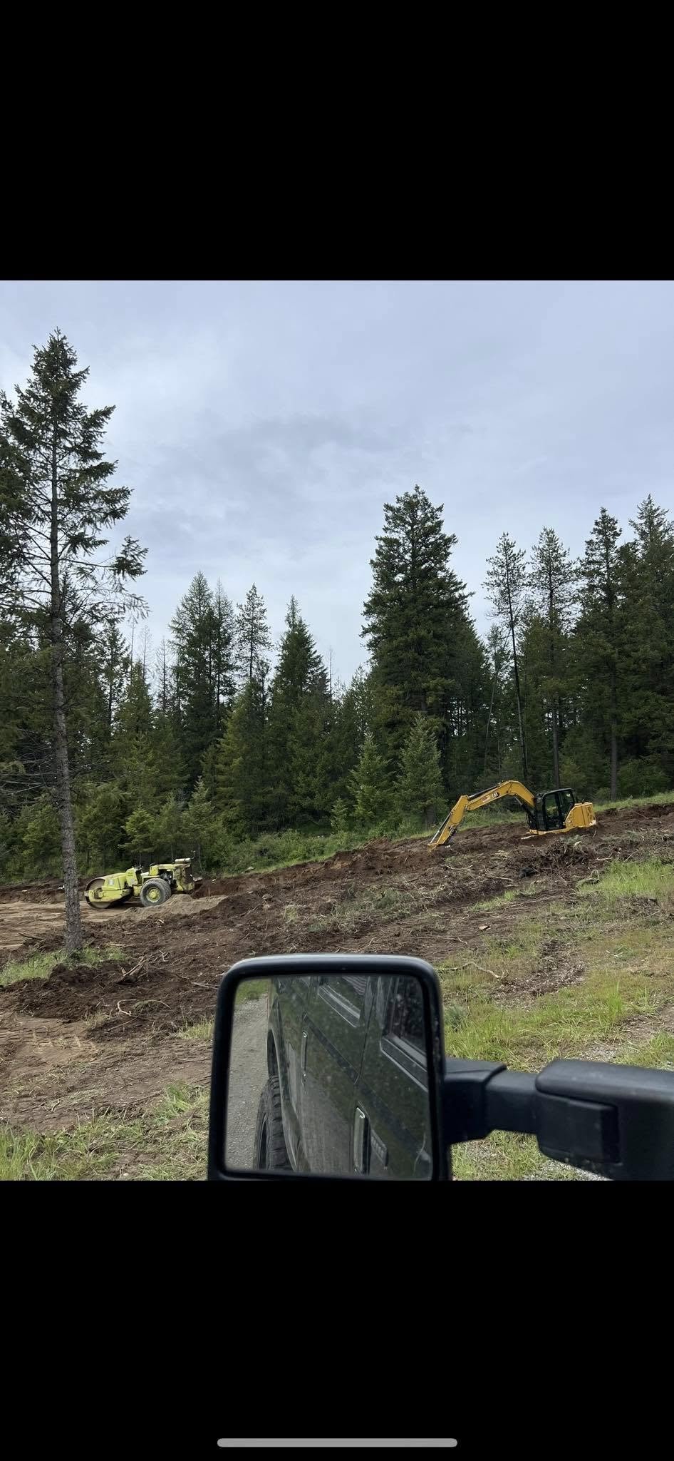 Excavator and roller on hillside site prep job